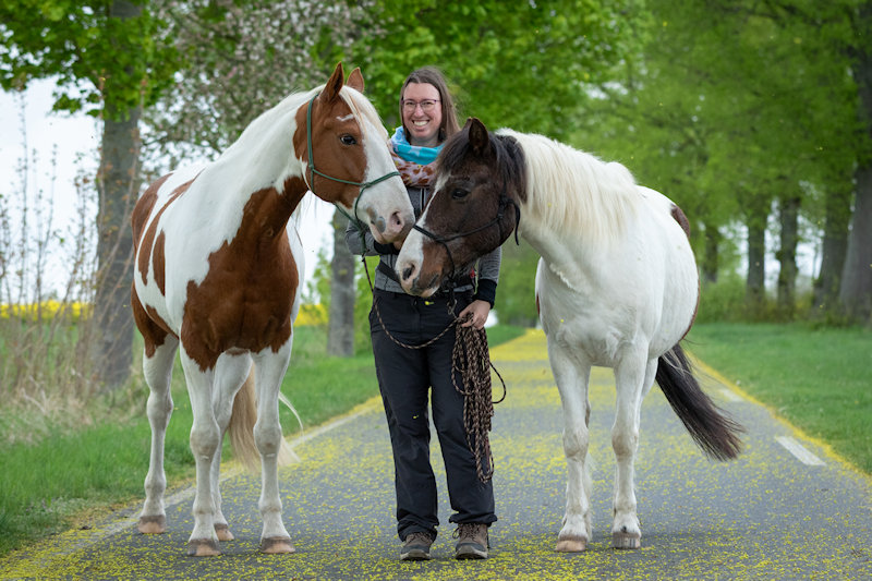 Foto von Jessica mit Jack und Janek auf einer Allee. Jessica trägt Outdoorklamotten und ein buntes Tuch.