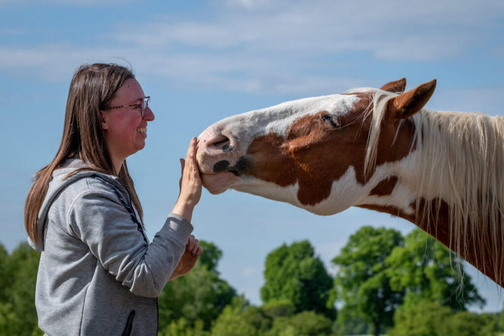 Autorin Jessica Freymark und ihr Pflegepferd Jack, der seine Nase in ihre Hand drückt.